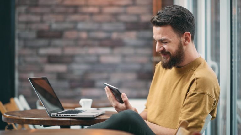 Junger Mann nutzt im Café den Google Authenticator auf mehreren Geräten