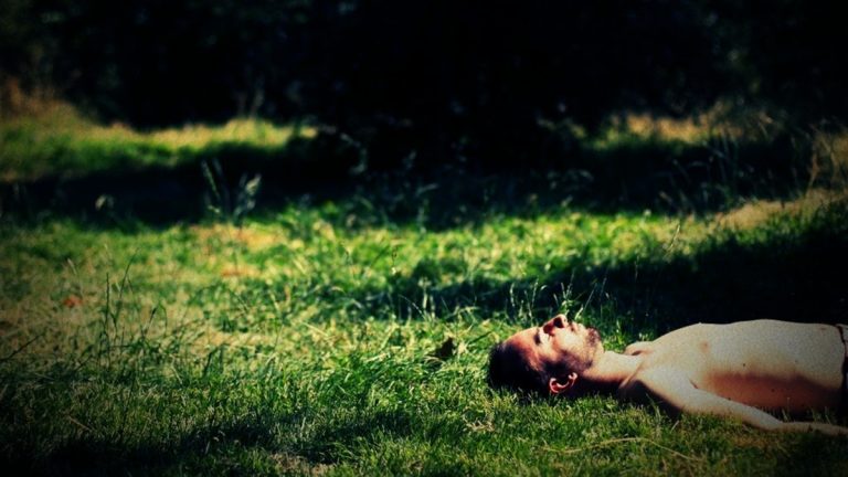 Mann liegt an sonnigem Tag im Gras und wird mit Lomo-Kamera fotografiert