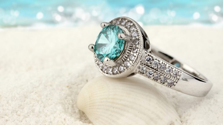 Schmuck fotografieren: Hintergründ und Accessoires Ring mit Aquamarin im Sand mit Muschel vor Meereshintergrund