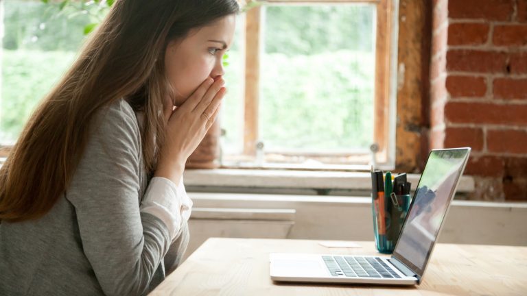 Junge Frau sieht erschrocken auf den Laptop-Bildschirm und überlegt, wie sie eine E-Mail zurückholen kann