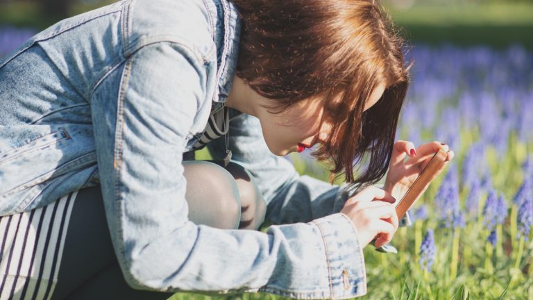 Junge Frau fotografiert Blumen mit dem Smartphone