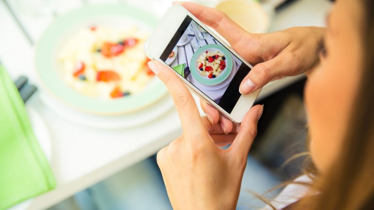 Instagram-Daten schützen: Junge Frau fotografiert ihr Essen mit dem Smartphone