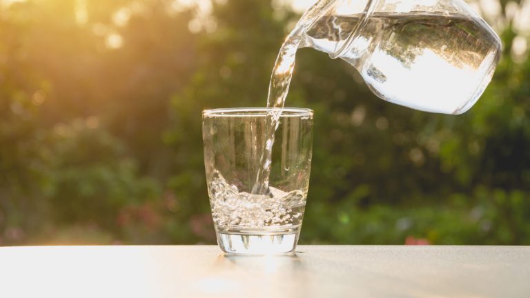 Wasser aus Trinkwassersprudler mit Flasche in Glas gießen
