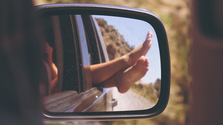 Im Rückspiegel fotografierte Füße, die aus dem Autofenster ragen