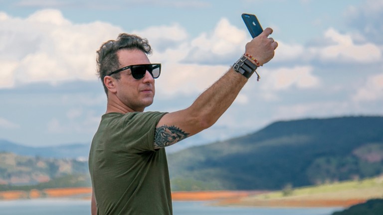 Mann vor Naturkulisse knipst Selfie mit Smartphone