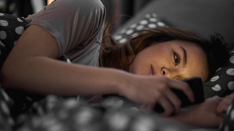 Frau liegt im Bett und sieht auf Smartphone mit gelblichem Licht
