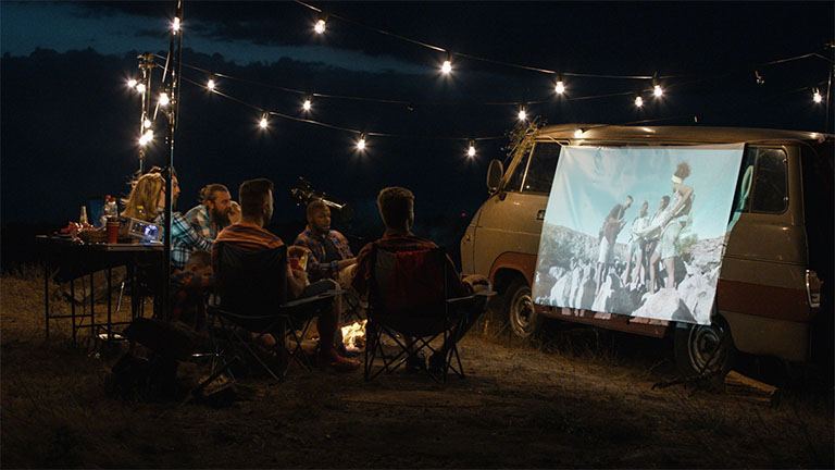 Freunde nutzen einen Beamer, um auf einem Campingbus einen Film zu schauen