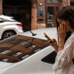 Frau mit Smartphone vor geparktem Auto