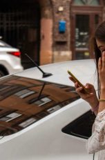Frau mit Smartphone vor geparktem Auto
