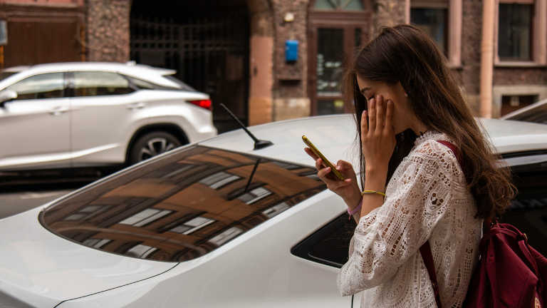 Frau mit Smartphone vor geparktem Auto