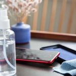 Ein iPhone SE in roter Farbe liegt auf dem Tisch. Daneben sind eine Schutzh&uuml;lle, eine Spr&uuml;hflasche und ein Mikrofasertuch zu sehen.