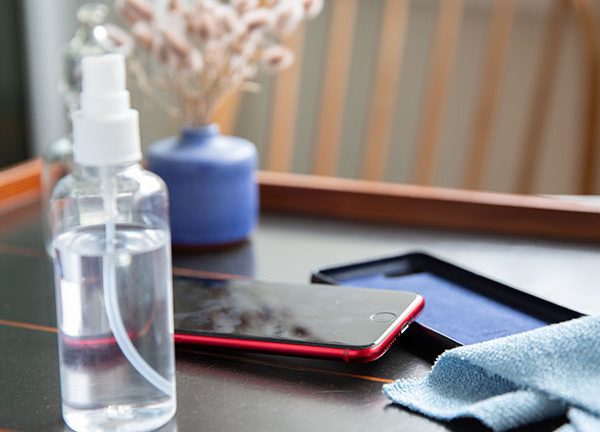 Ein iPhone SE in roter Farbe liegt auf dem Tisch. Daneben sind eine Schutzh&uuml;lle, eine Spr&uuml;hflasche und ein Mikrofasertuch zu sehen.