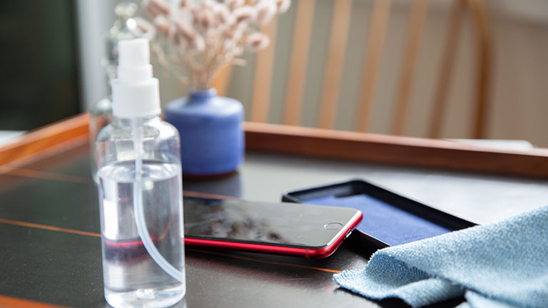Ein iPhone SE in roter Farbe liegt auf dem Tisch. Daneben sind eine Schutzhülle, eine Sprühflasche und ein Mikrofasertuch zu sehen.
