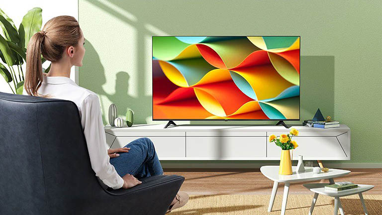 Eine Person sitzt im Sessel und blickt auf einen Fernseher von Hisense. Der zeigt ein Testvideo für die Farbkraft des Displays.