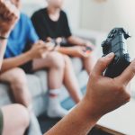 Mehrere Personen sitzen in einem Zimmer und haben PS4-Controller in der Hand.