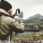 Ein Wanderer steht vor einem Berg. Mit seinem Smartphone nimmt er ein Bild der Szenerie auf.