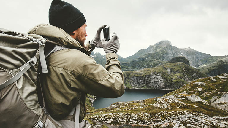 Ein Wanderer steht vor einem Berg. Mit seinem Smartphone nimmt er ein Bild der Szenerie auf.
