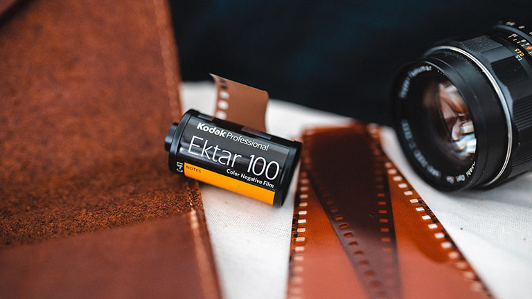 Ein analoger Film von Kodak neben einer analogen Kamera. Dazwischen liegen einige unbelichtete Filmstreifen.