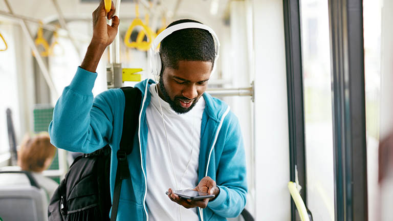 Eine Person steht im Bus und schaut auf dem Smartphone ein Video.