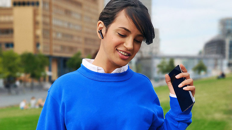 Eine Person hält das Vivo X51 5G in der Hand. Sie steht draußen und telefoniert über Kopfhörer.