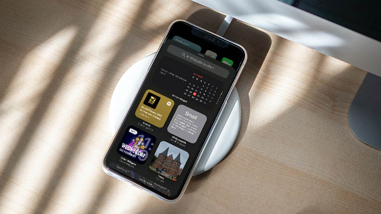 Ein iPhone auf einer kabellosen Ladestation. Auf dem Bildschirm ist die neue Auswahl der Widgets zu sehen.