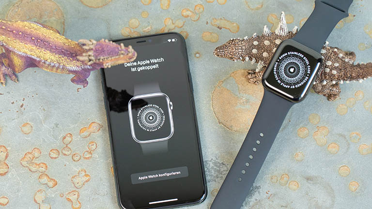 Apple Watch und iPhone liegen neben zwei Spielzeug-Dinosauriern nebeneinander. Auf den Display ist zu sehen, dass die Kopplung der Apple Watch erfolgreich war.
