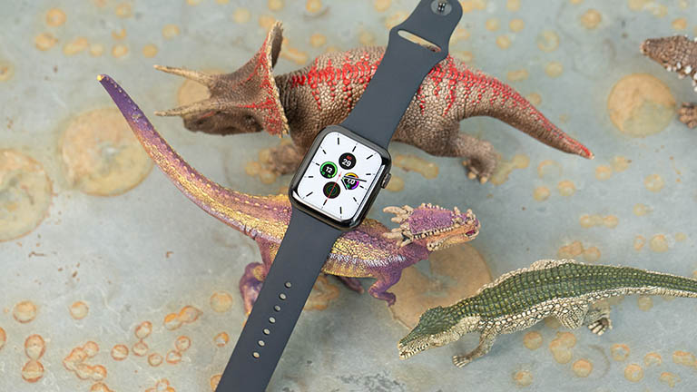 Die Apple Watch liegt auf Spielzeug-Dinosaurieren. Auf dem Display lässt sich ein weißes Ziffernblatt erkennen.