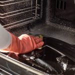 Eine Person mit Handschuhen wischt mit einem Schwamm den Backofen aus.