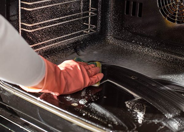Eine Person mit Handschuhen wischt mit einem Schwamm den Backofen aus.