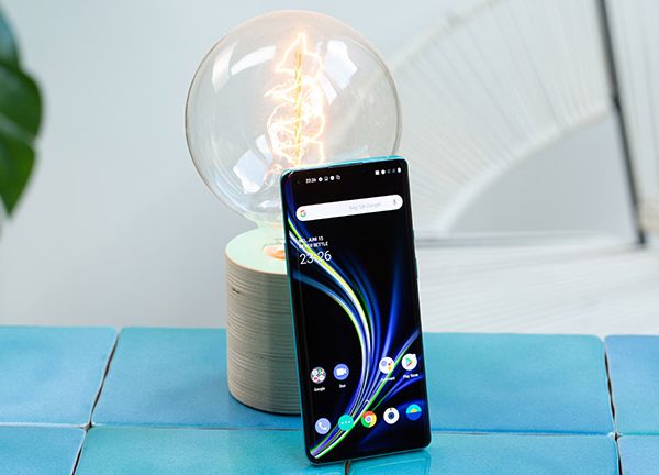 Das OnePlus 8 Pro steht aufrecht angelehnt an eine Gl&uuml;hbirne. Das Display ist aktiviert und zeigt den Home-Bildschirm.