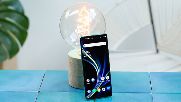 Das OnePlus 8 Pro steht aufrecht angelehnt an eine Glühbirne. Das Display ist aktiviert und zeigt den Home-Bildschirm.