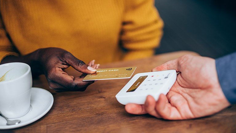 Eine Person hält eine Kreditkarte mit RFID-Technik in die Nähe eines Kartenlesegeräts.