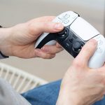 Eine Person h&auml;lt den DualSense-Controller der PlayStation 5 leicht schr&auml;g ins Bild.