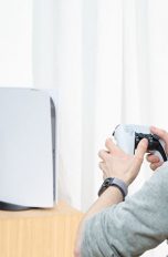 Eine Person sitzt vor einer PlayStation 5 und hält dabei den neuen DualSense-Controller in der Hand.