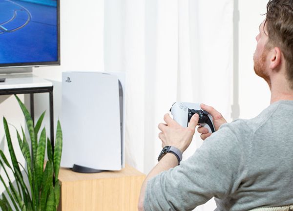 Eine Person sitzt vor einer PlayStation 5 und h&auml;lt dabei den neuen DualSense-Controller in der Hand.
