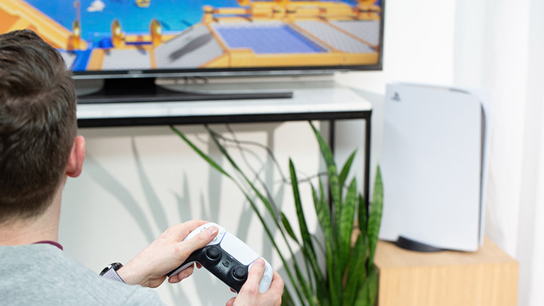 Eine Person sitzt vor einem Fernseher und spielt auf einer PlayStation 5.