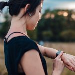 Eine junge Frau in kurzärmeligem T-Shirt steht in der Natur und bedient eine Apple Watch am Handgelenk.