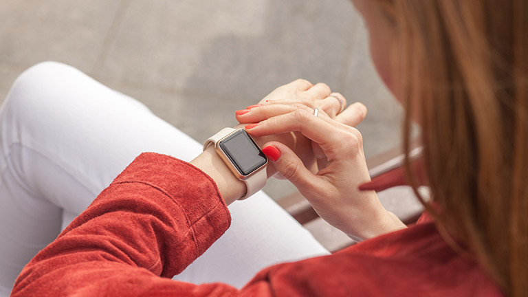Blick über die linke Schulter einer Frau, die gerade auf ihre Apple Watch am linken Handgelenk schaut.