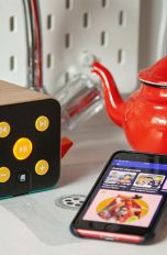 Ein Smartphone mit geöffneter Spotify-App und ein kindgerechter Lautsprecher in einer Spielküche.