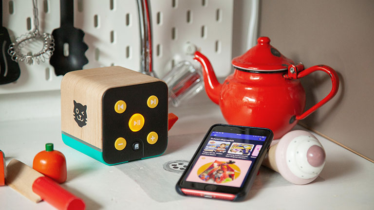Ein Smartphone mit geöffneter Spotify-App und ein kindgerechter Lautsprecher in einer Spielküche.