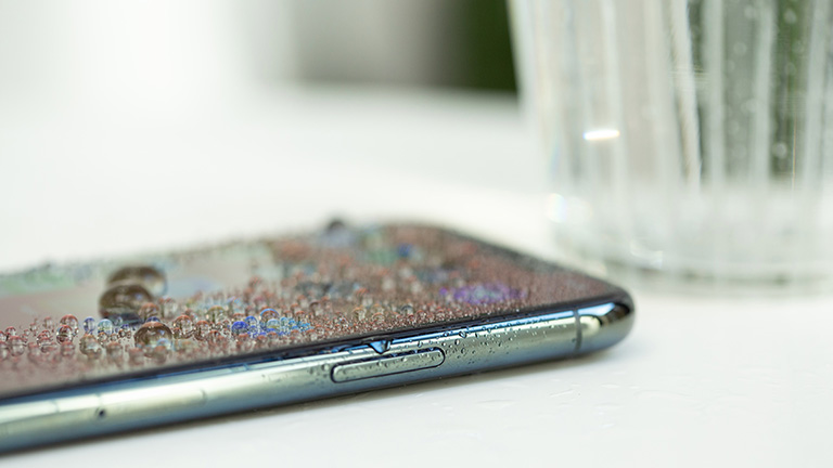 Das iPhone 11 ist mit Wasser bedeckt. Daneben steht ein Glas.