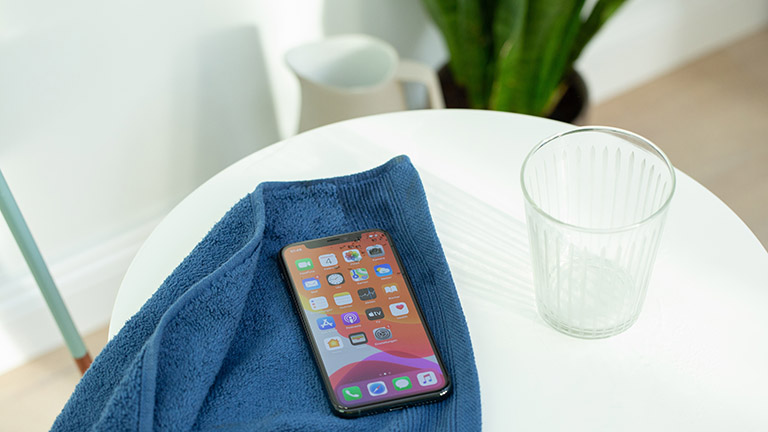 Ein iPhone 11 liegt auf einem Handtuch. Daneben steht ein Wasserglas.
