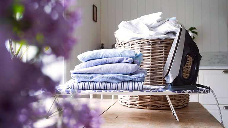Ein Bügeleisen steht auf einem kleinen Bügelbrett neben einem kleinen Stapel Wäsche.