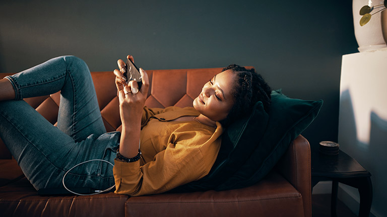 Eine Person liegt auf dem Sofa und spielt etwas auf dem Smartphone.