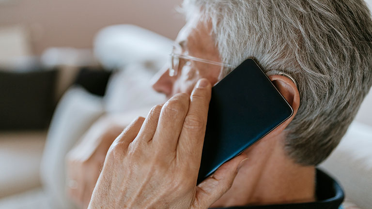 Eine ältere Person telefoniert mit einem Smartphone am Ohr.
