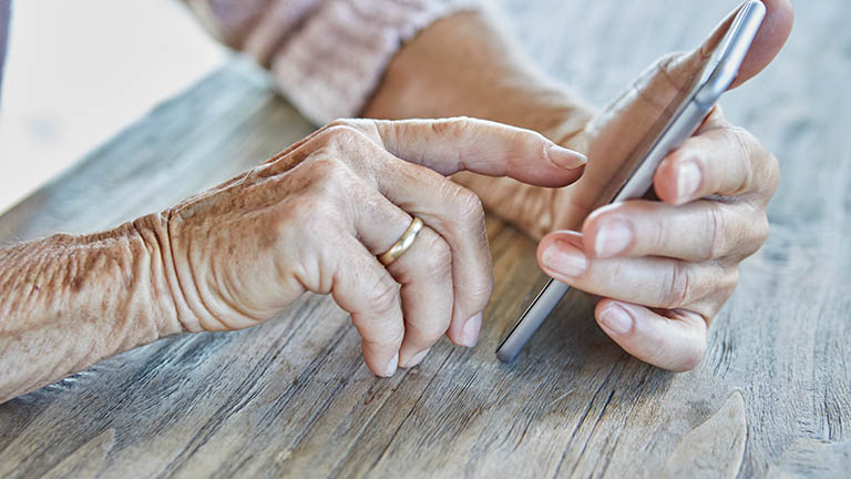 Eine ältere Person bedient mit dem Finger das Touch-Display eines Smartphones.