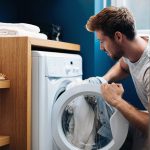 Ein Mann kniet vor einer geöffneten Waschmaschine und steckt Wäsche hinein.