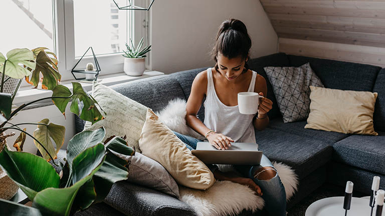 Eine Person sitzt auf dem Sofa und bedient ein MacBook.