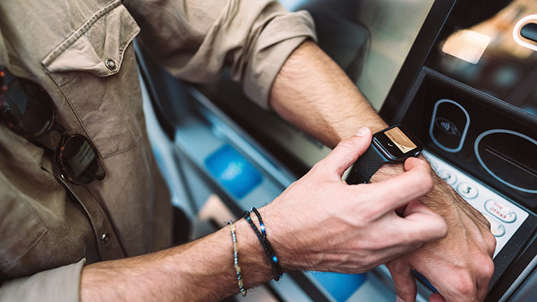 Eine Person hält ihre Apple Watch an ein Kartenlesegerät, um damit den Transport im öffentlichen Verkehr zu bezahlen.