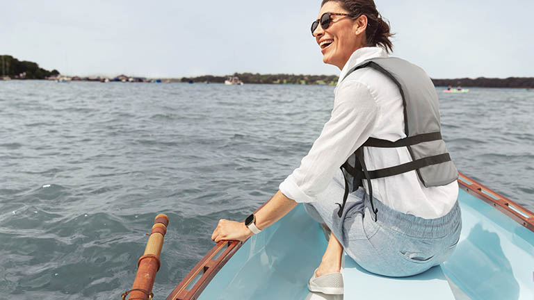 Eine Person sitzt in einem Ruderboot. Am Handgelenk trägt sie eine Fitbit Sense.
